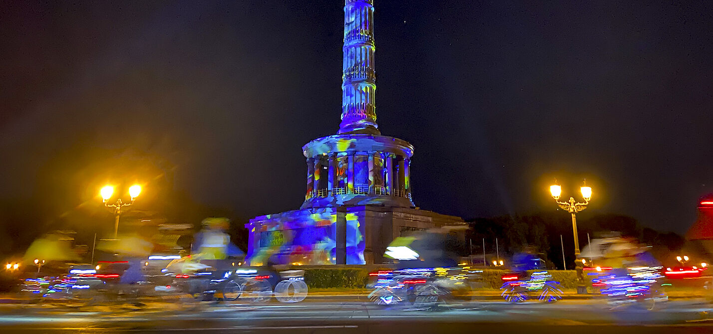 Lichterfahrt 2024 Menschen auf Fahrrädern fahren im Dunklen um die bunt angestrahlte Siegessäule