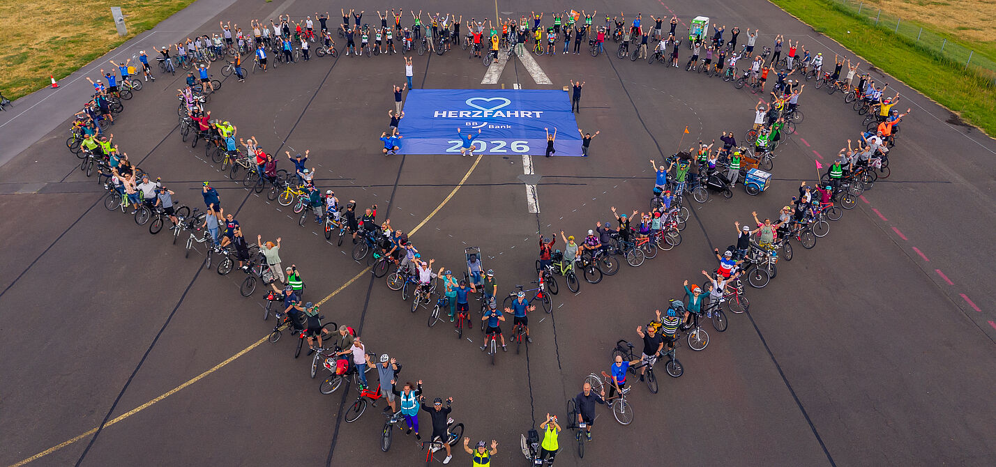 Menschen mit Fahrrädern bilden zwei Herzen um HerzFahrt Banner auf dem Boden