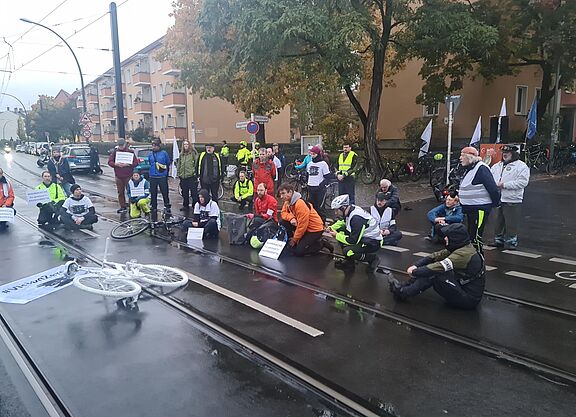 Mahnwache 23-10-27 Menschen sitzen bei einer Mahnwache auf der Straße um ein weißes Geisterrad