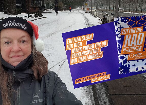 Stadtteilgruppe Mitte - Nikolaus Aktion Die Fotomontage zeigt SuSanne Grittner auf der Seestraße mit einer Postkarte, an der eine lila und weiß bedruckte Plastikverpackung angeheftet ist.