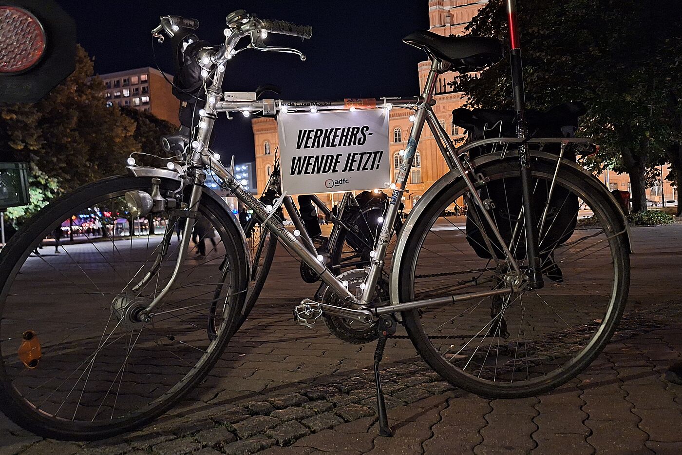 Lichterfahrt 2024 ein silbernes Fahrrad mit Lichterkette und Schild auf dem steht: Verkehrswende jetzt