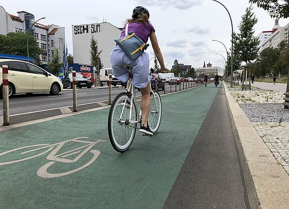 Radfahrstreifen Eine Frau fährt auf einem grün markierten Radfahrstreifen mit Pollern vom Autoverkehr getrennt.