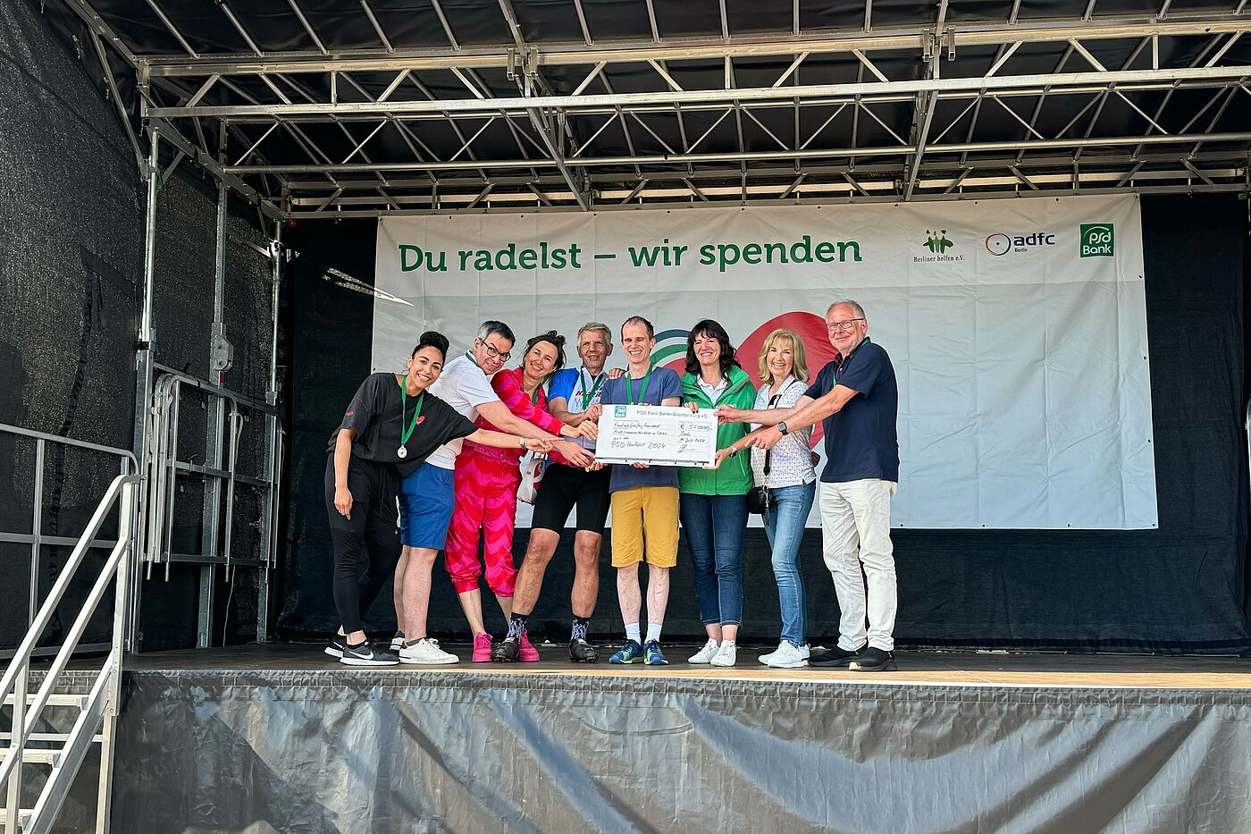 PSD Herzfahrt 2024 Ein Spendencheck wird von mehreren Menschen auf einer Bühne überreicht