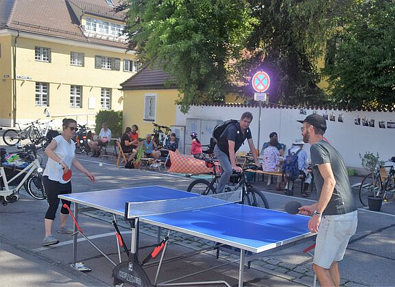 Tischtennispartie und Menschen im Hintergrund, die am Straßenrand sitzen.
