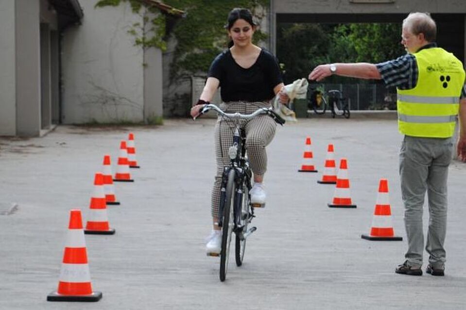 Übung Radfahrschule Frau fährt mit Fahrrad und nimmt Tuch von Lehrer entgegen